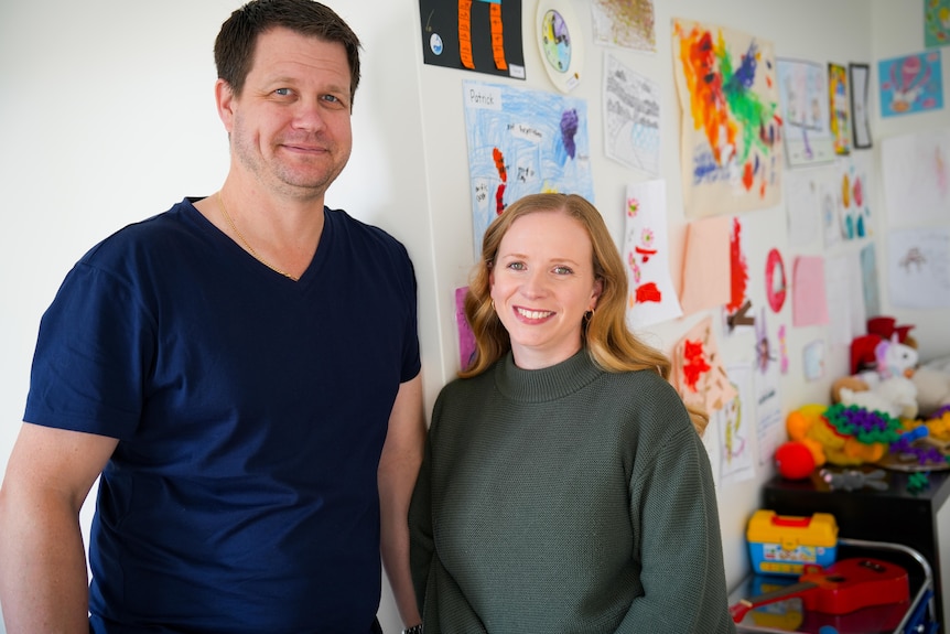 Warren and Christine smile in front of a wall covered in their children's drawings.