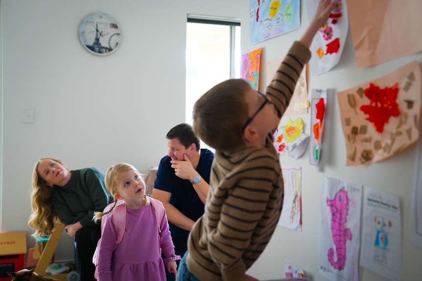 Patrick reaches a colorful picture on the wall with his parents sitting behind him.