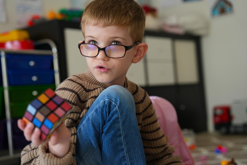 A cute child wearing glasses plays with a Rubik's cube.